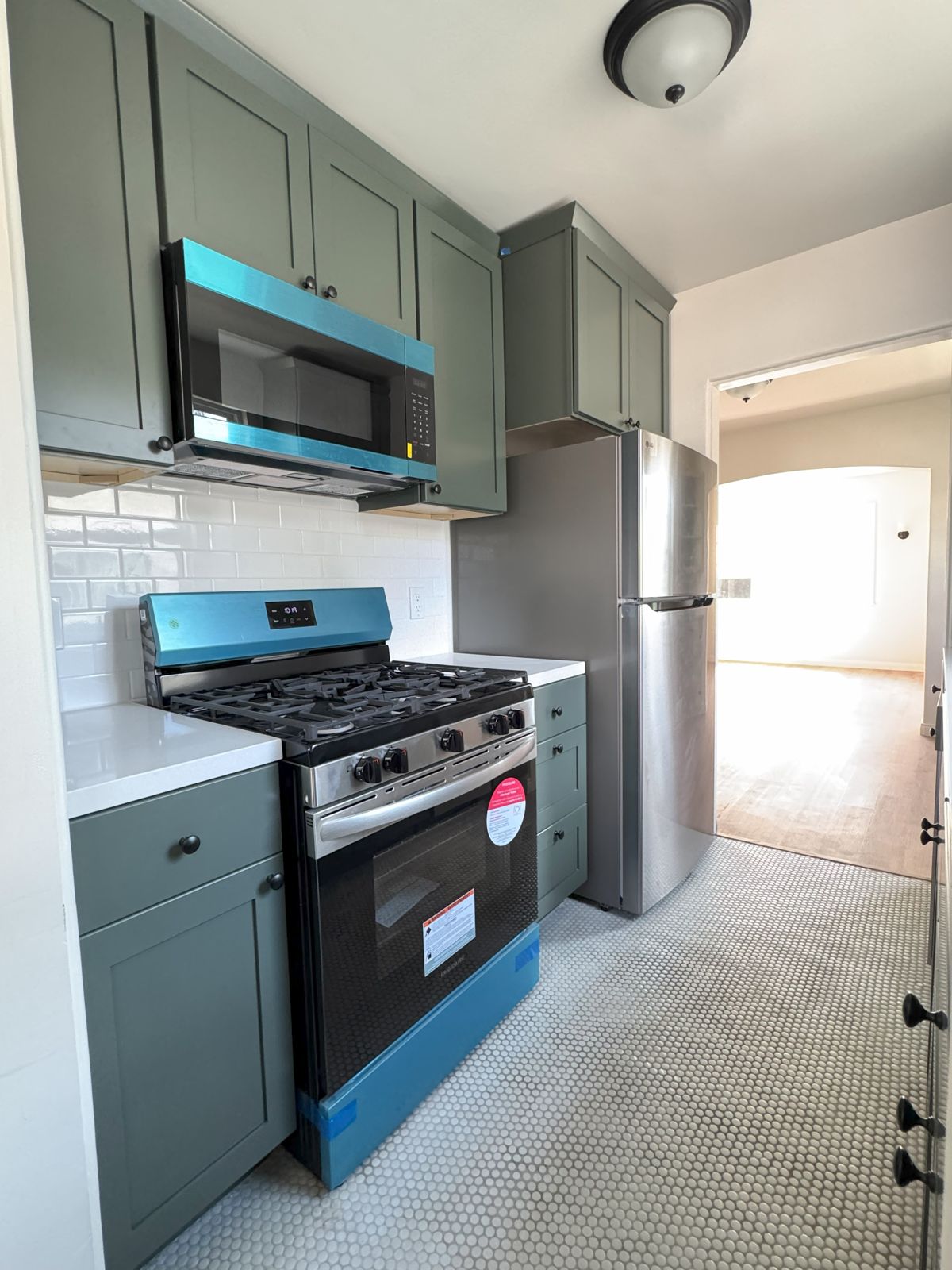 Kitchen with dark green cabinets, gas range and stainless refrigerator